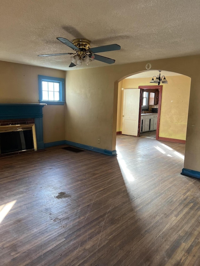 unfurnished living room with baseboards, ceiling fan with notable chandelier, a fireplace, wood finished floors, and arched walkways