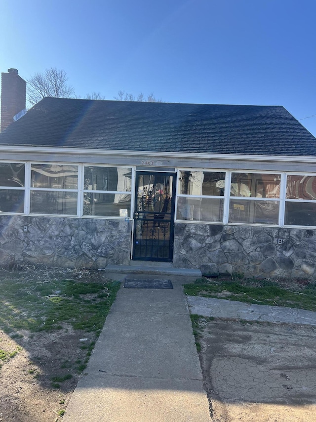 doorway to property with stone siding, roof with shingles, and a chimney