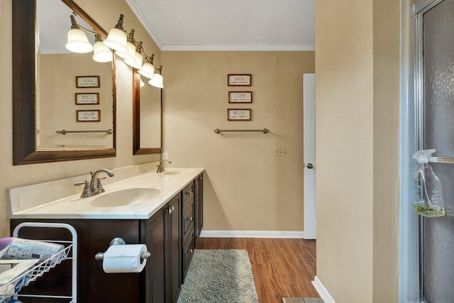 bathroom with ornamental molding, a sink, a textured ceiling, wood finished floors, and double vanity