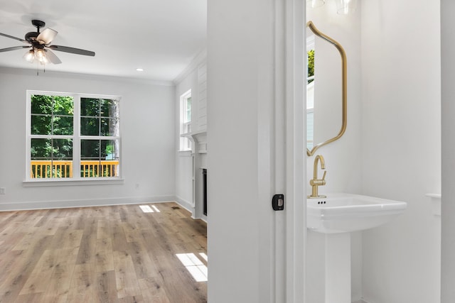 interior space featuring wood finished floors, a ceiling fan, baseboards, a fireplace, and crown molding