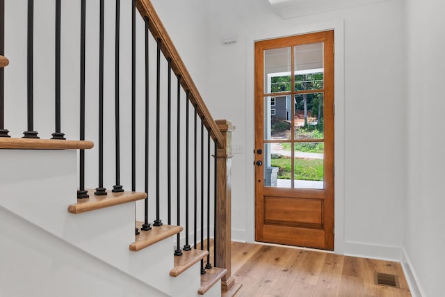 entryway with stairway, baseboards, light wood-style floors, and visible vents