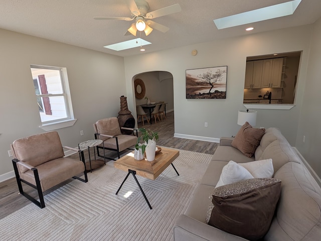 living area featuring wood finished floors, a ceiling fan, baseboards, a skylight, and arched walkways