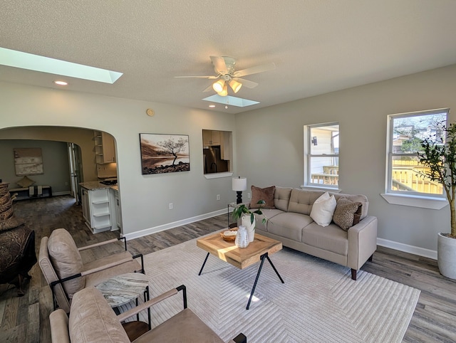 living room featuring arched walkways, a skylight, a ceiling fan, and dark wood-style flooring