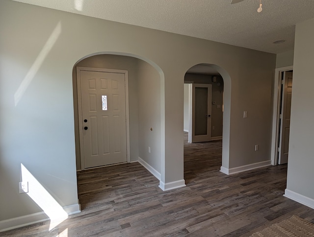 entrance foyer featuring dark wood finished floors, baseboards, arched walkways, and a textured ceiling