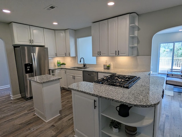 kitchen with open shelves, black gas cooktop, stainless steel refrigerator with ice dispenser, arched walkways, and a sink