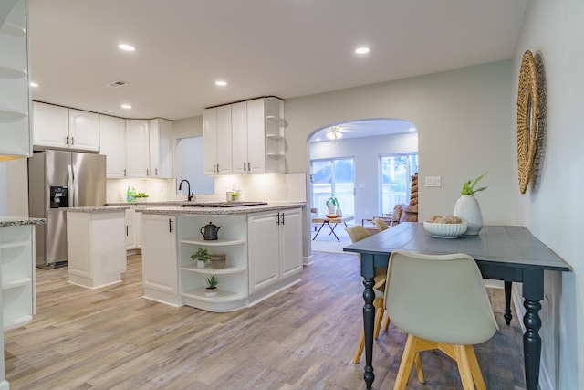 kitchen featuring arched walkways, a kitchen island, stainless steel refrigerator with ice dispenser, and open shelves