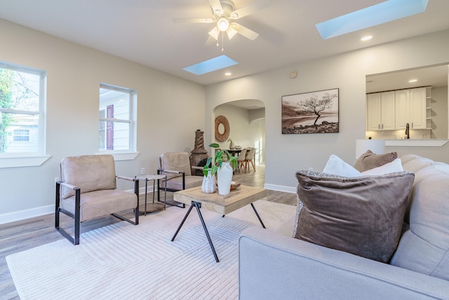 living area featuring baseboards, arched walkways, a skylight, and light wood finished floors