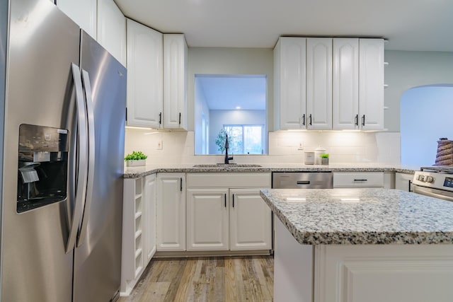 kitchen featuring a sink, light wood-type flooring, appliances with stainless steel finishes, arched walkways, and open shelves