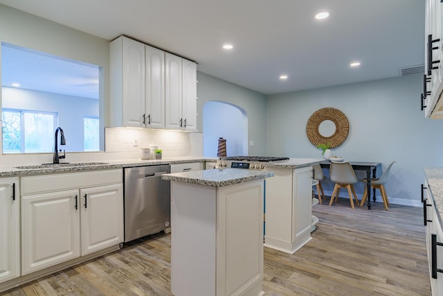 kitchen with a peninsula, light wood-style flooring, arched walkways, a sink, and stainless steel dishwasher