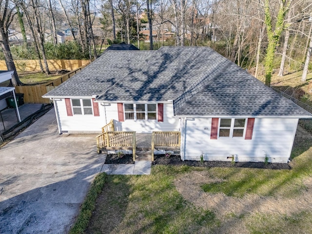 view of front facade with driveway, a shingled roof, and fence