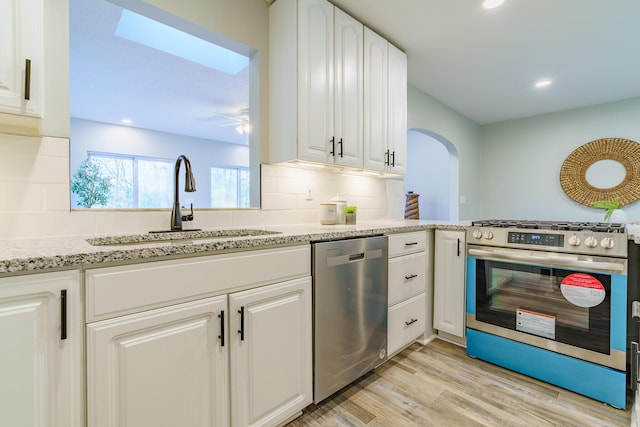 kitchen with tasteful backsplash, light wood-style flooring, arched walkways, stainless steel appliances, and a sink