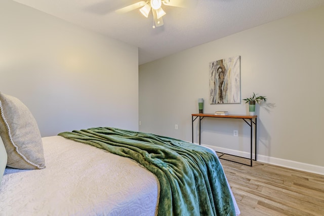 bedroom with light wood-type flooring, baseboards, a textured ceiling, and a ceiling fan