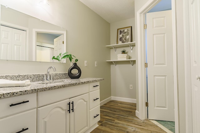 bathroom with a textured ceiling, vanity, baseboards, and wood finished floors