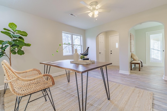 home office featuring light wood finished floors, visible vents, baseboards, arched walkways, and a ceiling fan