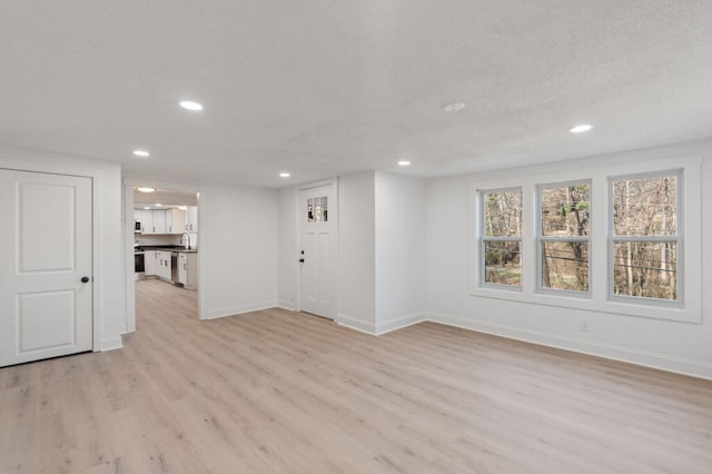 unfurnished living room with recessed lighting, light wood-style floors, baseboards, and a textured ceiling