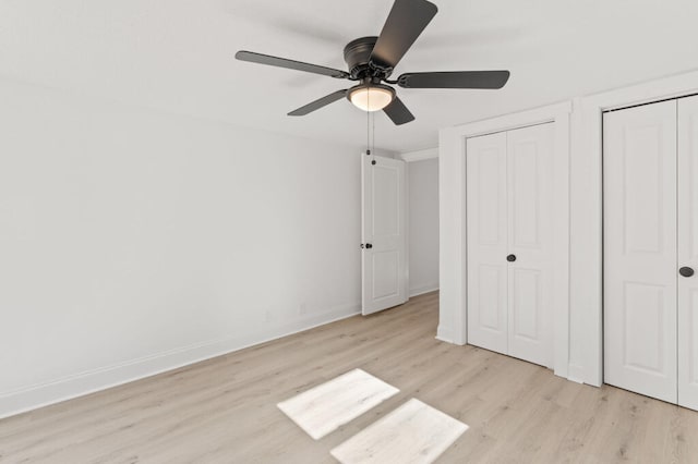 unfurnished bedroom featuring ceiling fan, baseboards, light wood-type flooring, and multiple closets