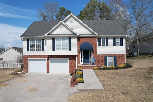 bi-level home featuring brick siding, a front lawn, fence, a garage, and driveway