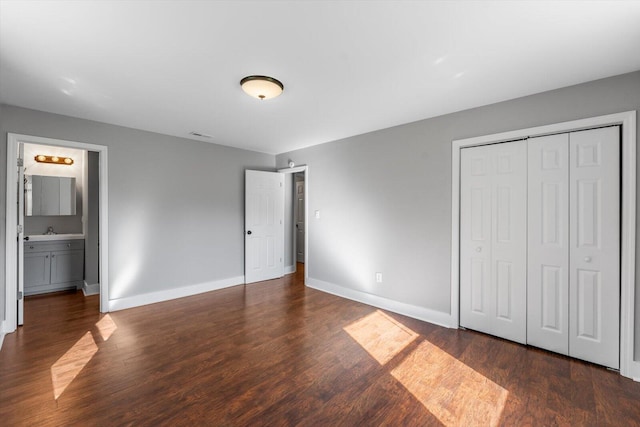 unfurnished bedroom with baseboards, wood finished floors, a closet, ensuite bath, and a sink