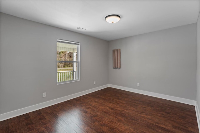 empty room featuring visible vents, dark wood-type flooring, and baseboards