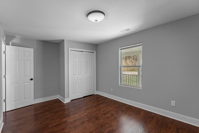 unfurnished bedroom with visible vents, baseboards, dark wood-style flooring, and a closet