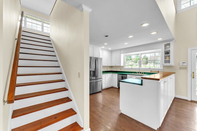 kitchen featuring stainless steel appliances, a sink, a peninsula, white cabinetry, and hardwood / wood-style flooring