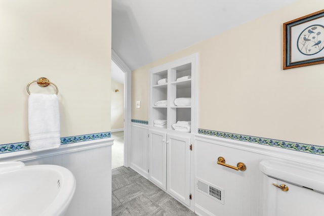 bathroom featuring built in shelves, a wainscoted wall, and a sink