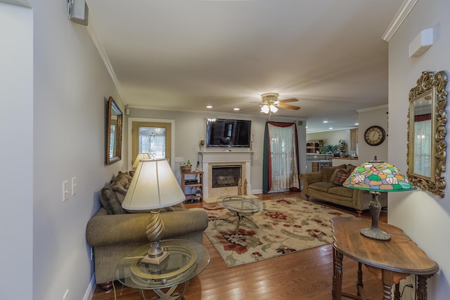 living room with a glass covered fireplace, wood finished floors, ornamental molding, and a ceiling fan