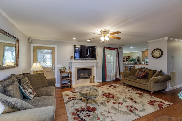 living room with a fireplace with raised hearth, ornamental molding, wood finished floors, recessed lighting, and ceiling fan