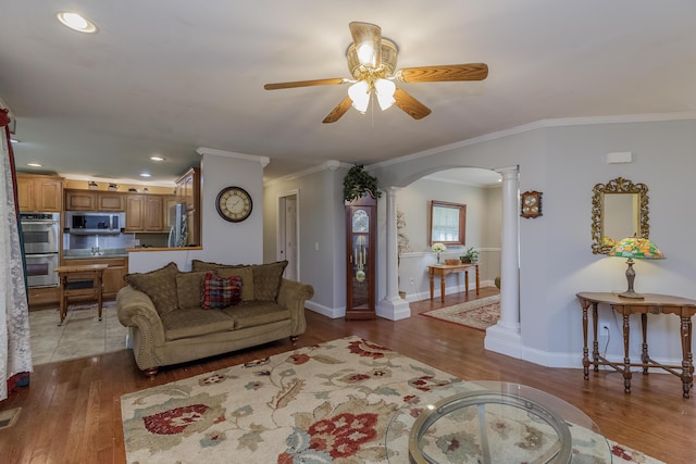 living room featuring wood finished floors, arched walkways, ornate columns, and ceiling fan