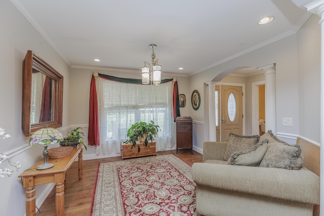 living area featuring wood finished floors, arched walkways, an inviting chandelier, decorative columns, and baseboards