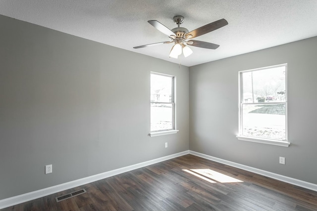 empty room featuring a ceiling fan, dark wood-style floors, visible vents, baseboards, and a textured ceiling