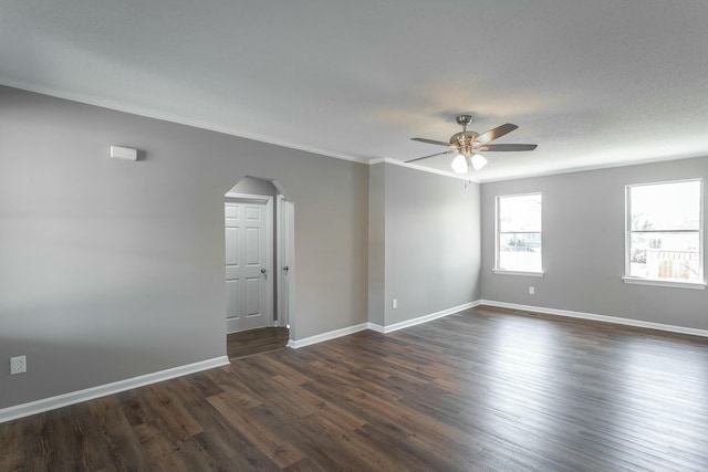 spare room with a ceiling fan, dark wood finished floors, arched walkways, crown molding, and baseboards