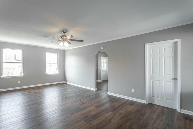 empty room featuring crown molding, baseboards, dark wood finished floors, arched walkways, and a ceiling fan