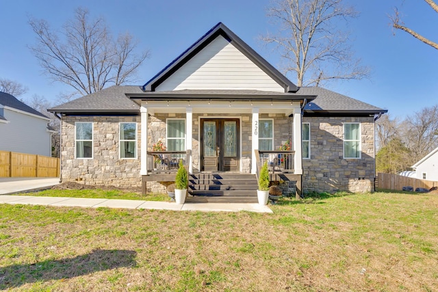 view of front facade with a front yard, fence, a porch, french doors, and stone siding