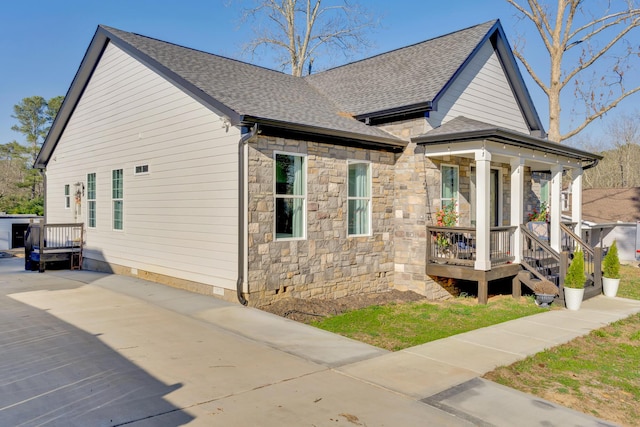 view of side of home with crawl space, stone siding, covered porch, and a shingled roof