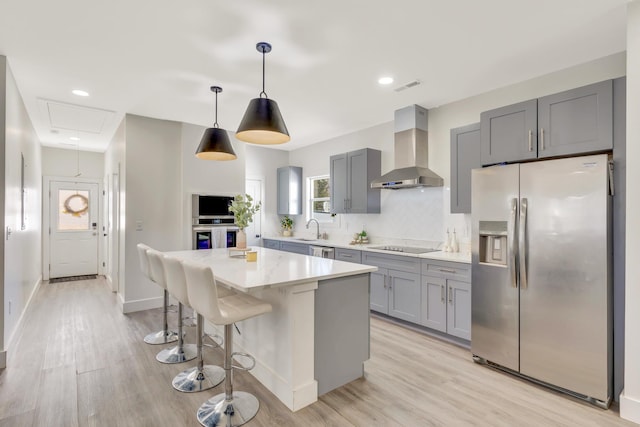 kitchen with gray cabinets, a sink, stainless steel appliances, wall chimney exhaust hood, and backsplash