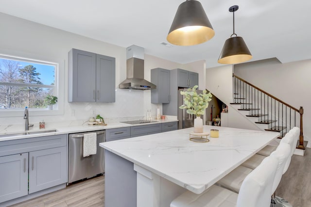 kitchen with a kitchen island, gray cabinets, stainless steel appliances, wall chimney exhaust hood, and a sink