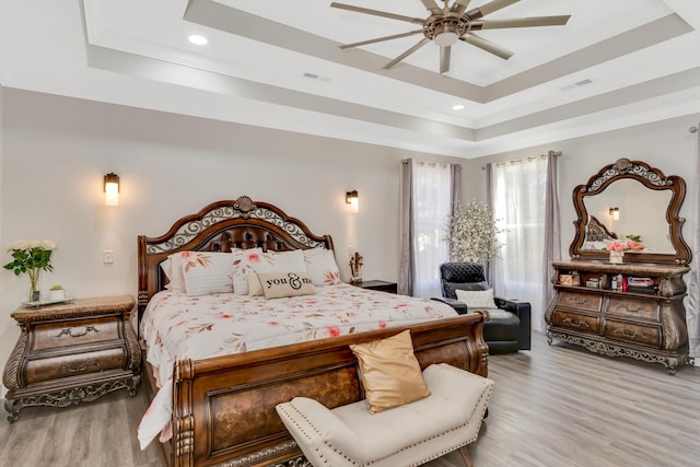 bedroom with a tray ceiling, wood finished floors, visible vents, and ornamental molding