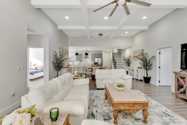 living room with beamed ceiling, coffered ceiling, stairway, light wood finished floors, and ceiling fan