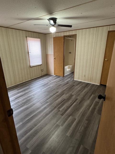 unfurnished bedroom featuring ceiling fan, a textured ceiling, dark wood-style floors, and wallpapered walls