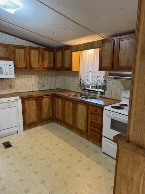 kitchen featuring white appliances, brown cabinetry, light floors, a sink, and vaulted ceiling