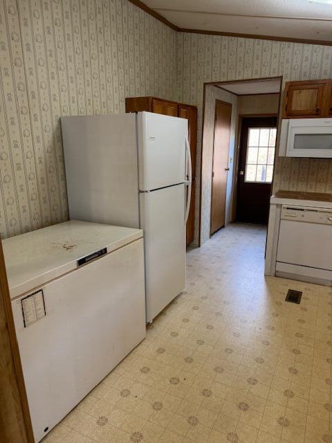 kitchen with white appliances, light floors, ornamental molding, and wallpapered walls