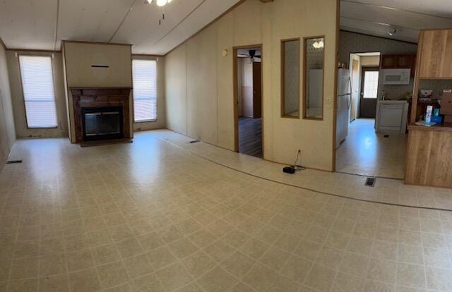 unfurnished living room featuring a glass covered fireplace, vaulted ceiling, light floors, and a wealth of natural light