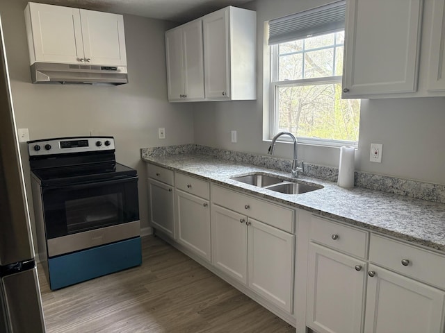 kitchen featuring under cabinet range hood, light wood-style flooring, stainless steel range with electric cooktop, white cabinetry, and a sink