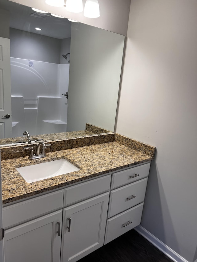 bathroom featuring visible vents, wood finished floors, baseboards, walk in shower, and vanity