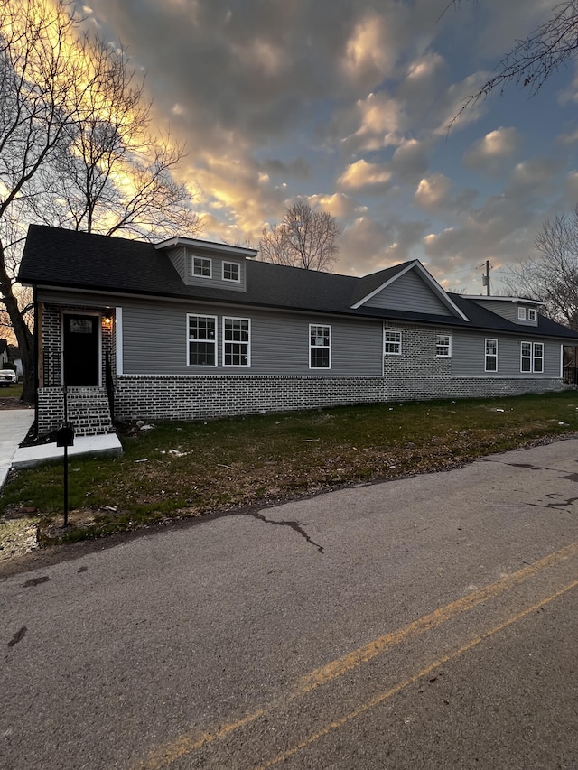 property exterior at dusk with brick siding and a lawn