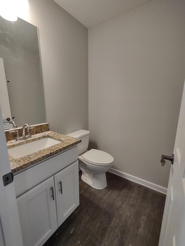 bathroom featuring baseboards, toilet, wood finished floors, and vanity