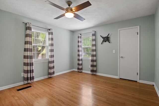 spare room with ceiling fan, a healthy amount of sunlight, visible vents, and wood finished floors