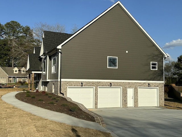 view of side of home featuring driveway, brick siding, an attached garage, and a shingled roof