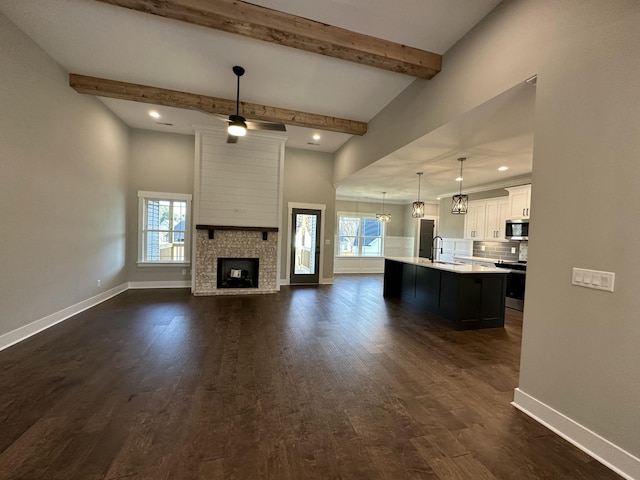 unfurnished living room featuring dark wood-type flooring, baseboards, beamed ceiling, a fireplace, and a sink